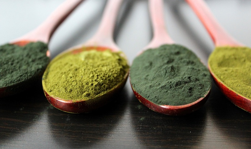 Assorted natural green superfood powder and spirulina tablets on a light background
